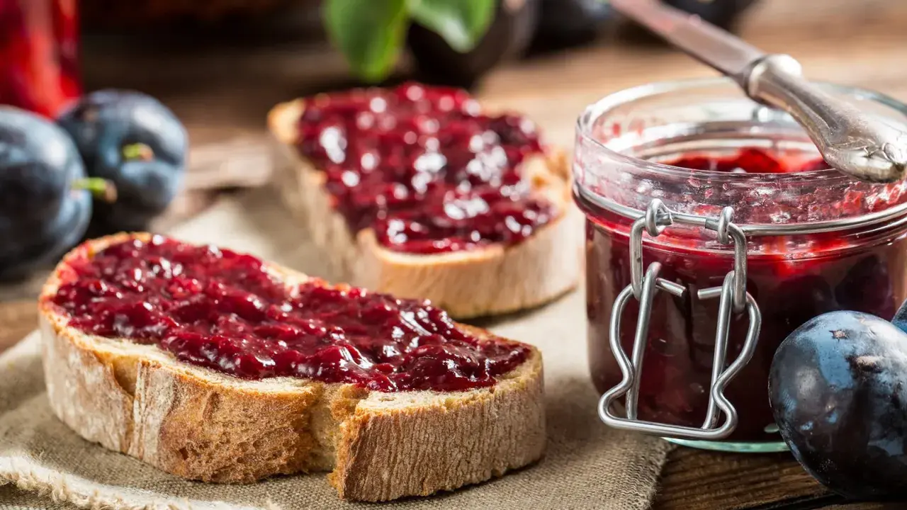 Frisches Brot mit Pflaumenmarmelade ohne Zucker, daneben eine Einmachglas gefüllt mit der leckeren Marmelade und frische Pflaumen.