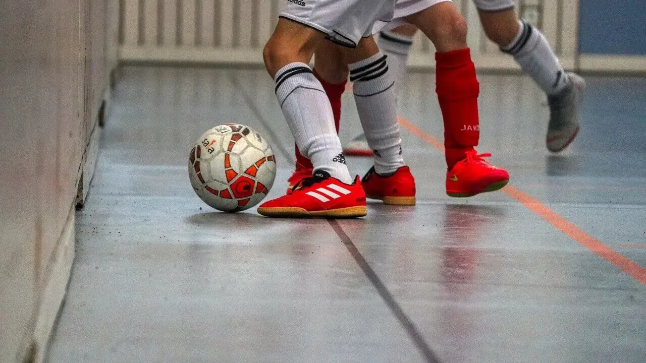 Piłka do futsalu na hali, obok butów zawodników. Tak, w turfy można grać na hali, to właśnie futsal!