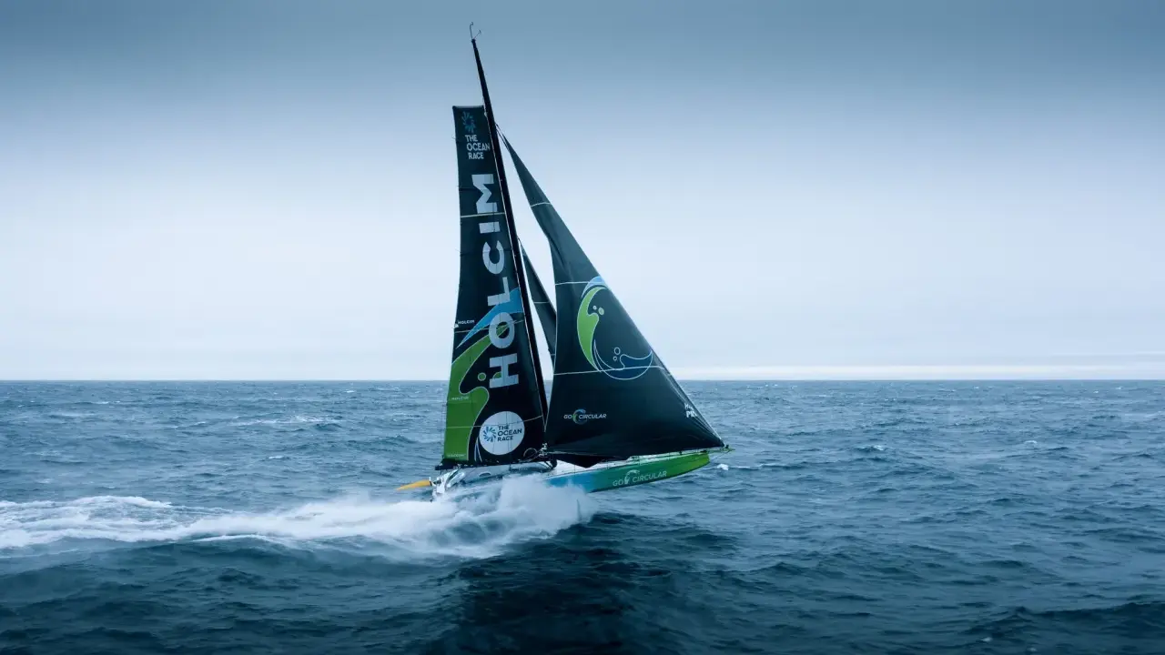 Segelboot des **Team Holcim** pflügt durch die Wellen, die Segel sind mit dem Logo und "The Ocean Race" beschriftet.