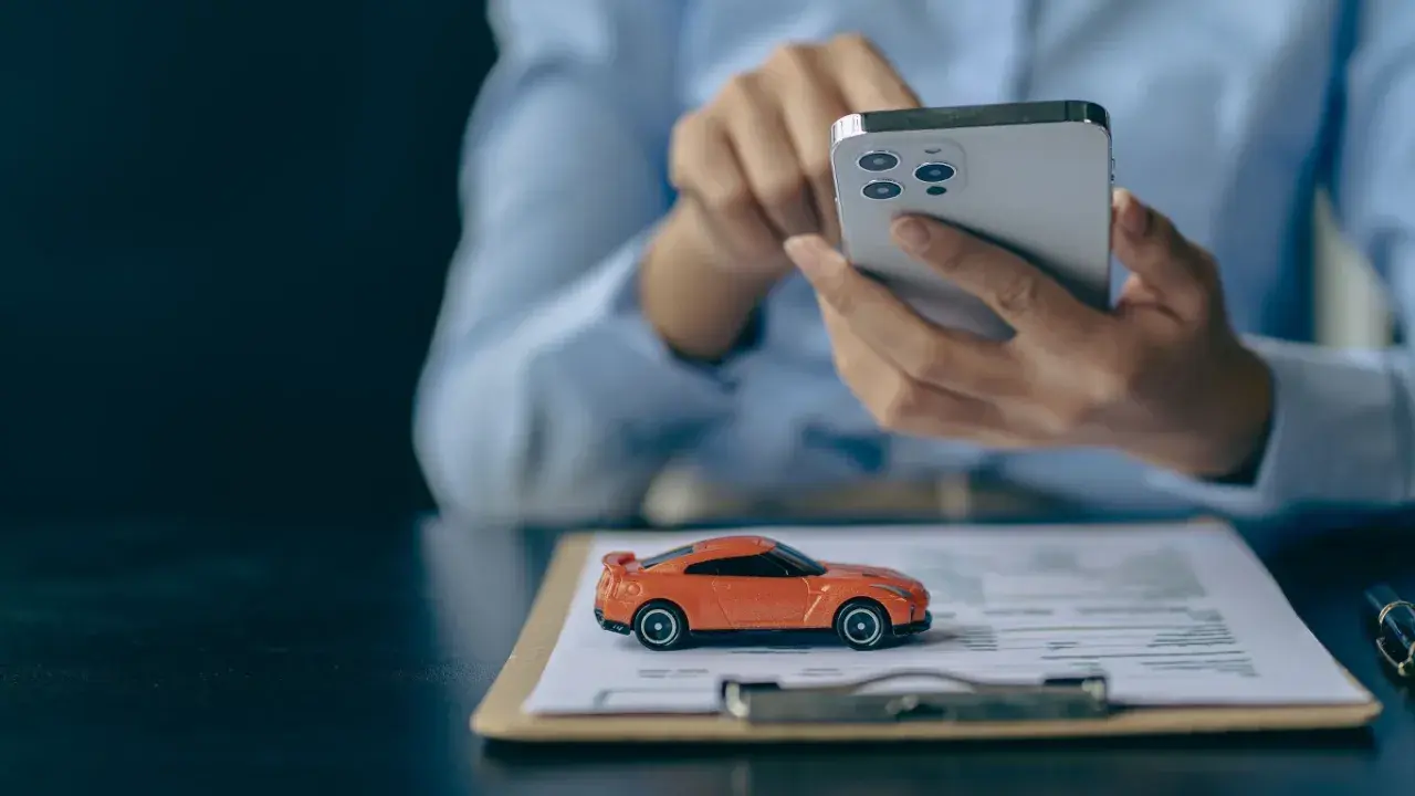 Pomarańczowy mini **casco** na dokumentach, obok dłoni trzymającej smartfon.