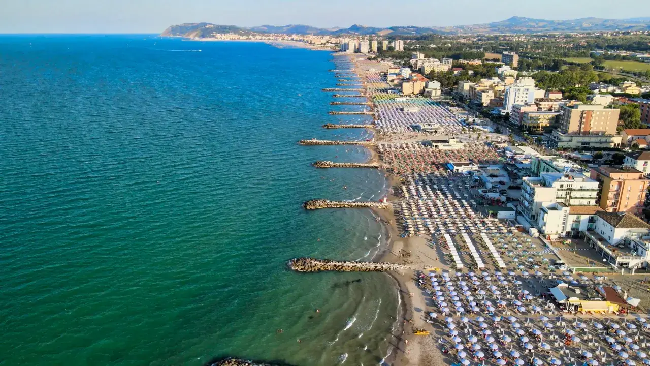 Vista aerea della costa adriatica, con la spiaggia affollata di ombrelloni e stabilimenti balneari, che si estende fino a Cattolica e Misano.