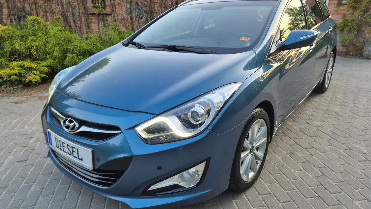 Niebieski Hyundai i40 1.7 CRDi na podjeździe z kostki brukowej, z tyłu ceglany mur porośnięty bluszczem.