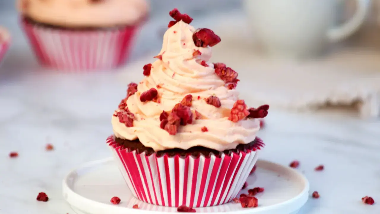 Ein köstlicher Red Velvet Muffin mit rosa Frosting und gefriergetrockneten Himbeeren, perfekt für ein Red Velvet Muffins Rezept.