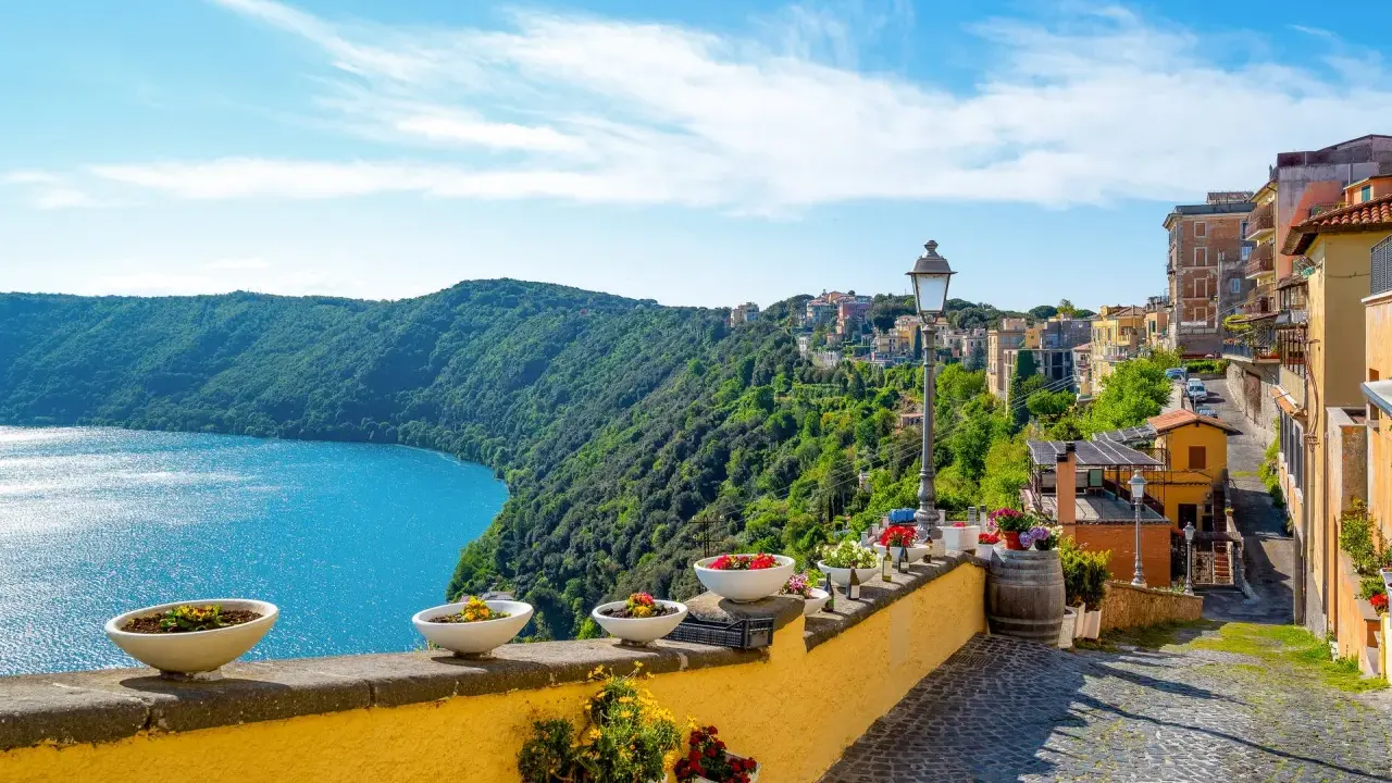 Widok na jezioro i zielone wzgórza z kolorowymi domami w Castel Gandolfo.