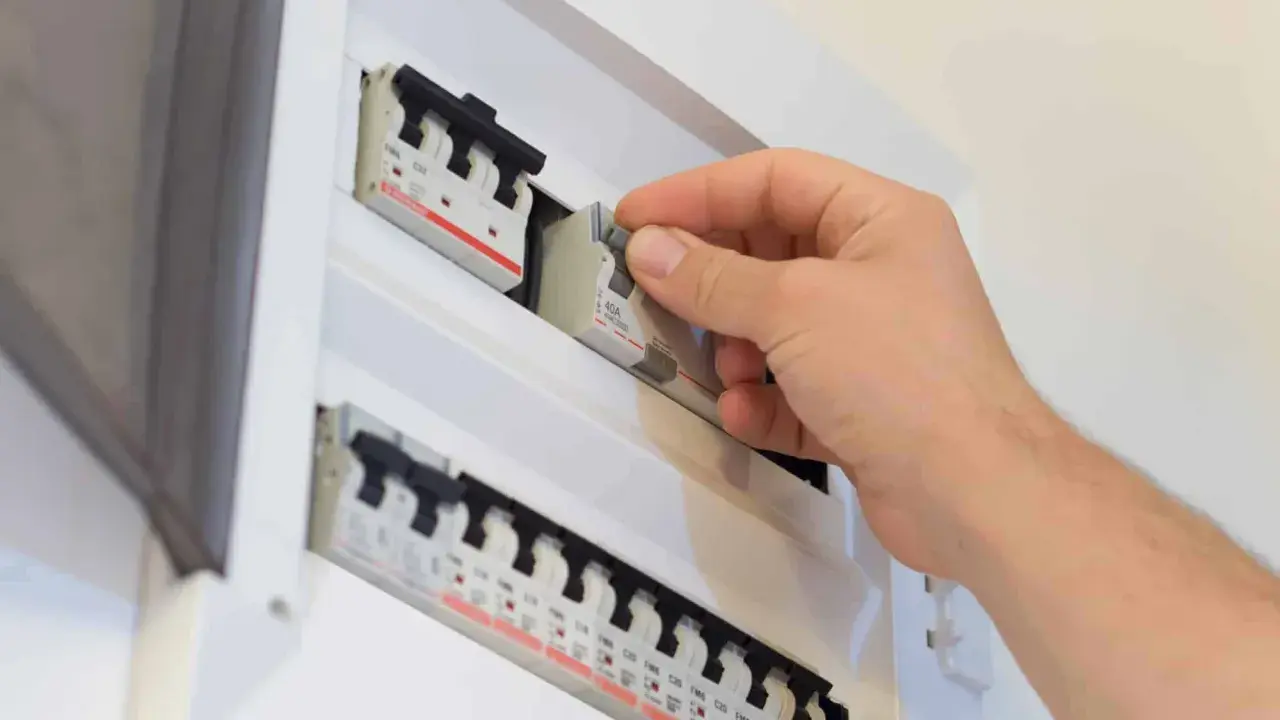 Main disjoncteur général manipulé par une main dans un tableau électrique blanc.