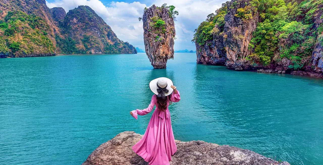 Donna con abito rosa e cappello bianco ammira la spettacolare **isola di James Bond** con le sue formazioni rocciose uniche e il mare turchese.