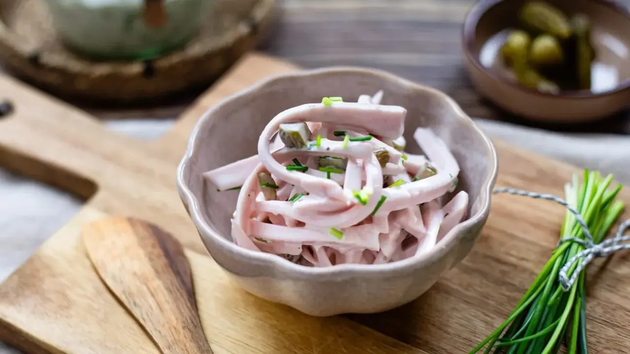 Schmackhaftes Fleischsalat Rezept mit Gurkenstückchen und Schnittlauch garniert, serviert in einer Schale auf einem Holzbrett.