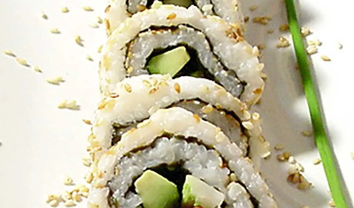 En närbild på en california roll med avokado och krabba, strödd med sesamfrön.