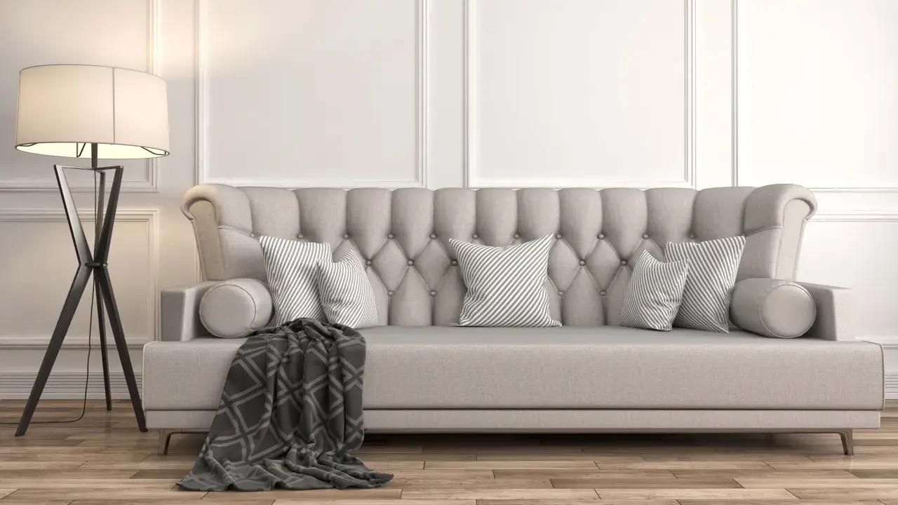 Divano imbottito grigio con cuscini a righe e coperta geometrica. La luce soffusa di una lampada da terra illumina la scena, dimostrando come grigio e beige stiano bene insieme.