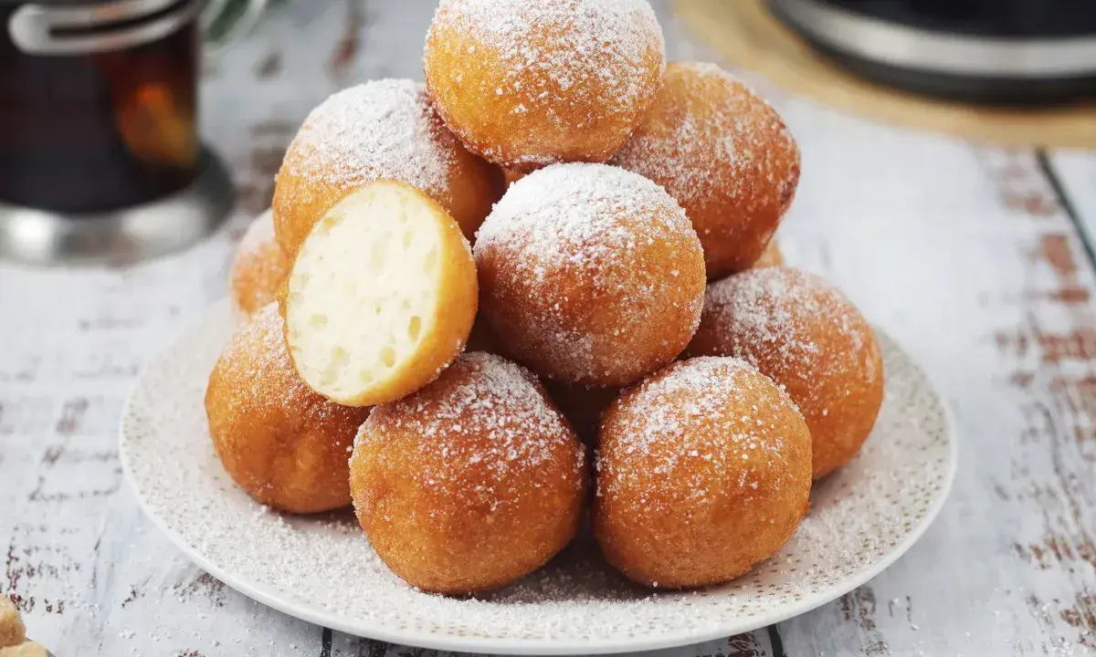 Puszyste pączki z piekarnika, posypane cukrem pudrem, kuszą swoim wyglądem. Jeden przekrojony ukazuje idealnie wyrośnięte wnętrze.