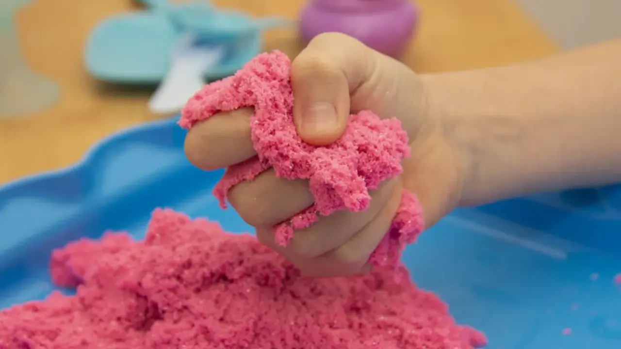 Kind hält pinken kinetischen Sand, der sich leicht formen lässt. Perfekt zum **kinetic sand selber machen** und Spielen.