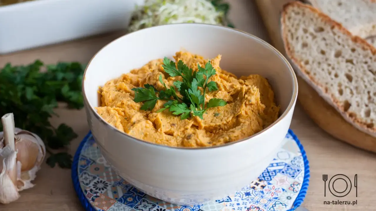 Pyszna pasta z kurczaka w miseczce, udekorowana natką pietruszki, obok czosnek i kromki chleba.