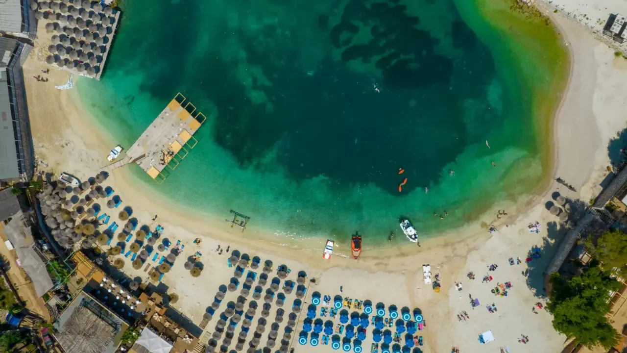 Widok z lotu ptaka na plażę z leżakami, parasolami i turkusową wodą.