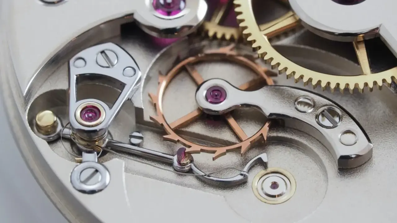 Meccanismo di orologio con ingranaggi dorati e ruota bilanciere, parte di uno scappamento coassiale.