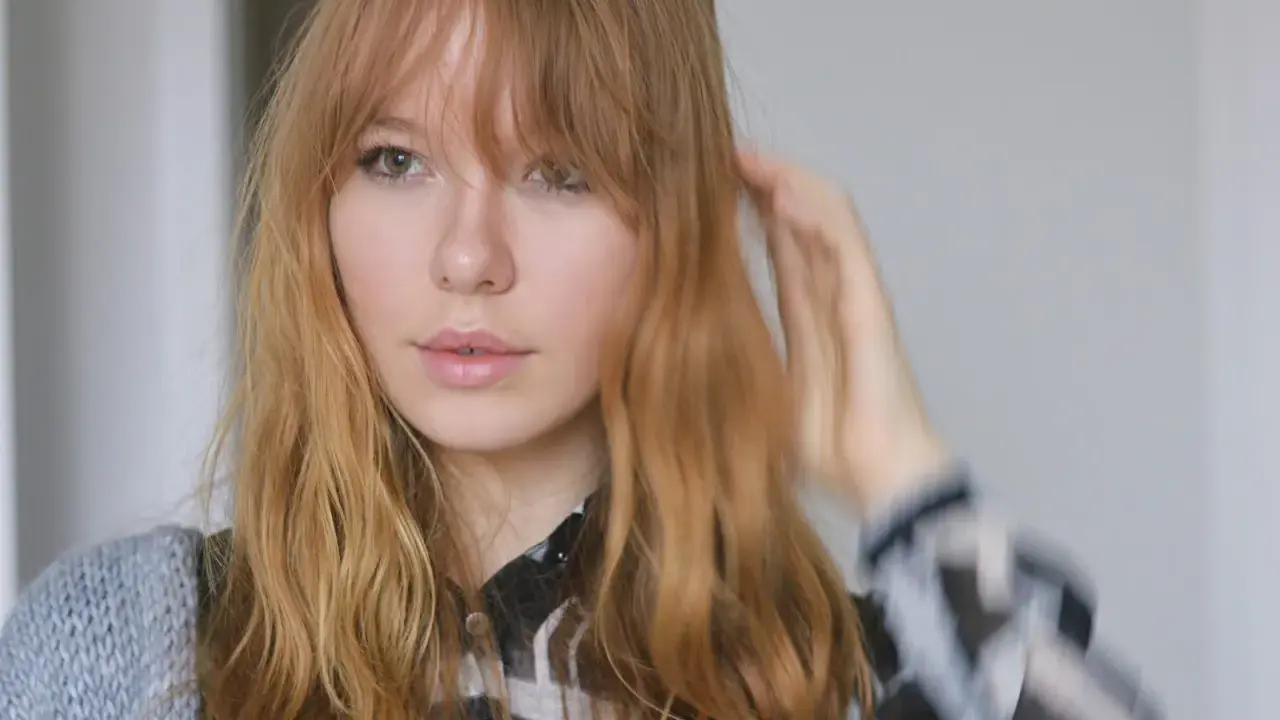 Ein junges Mädchen mit langen, welligen Haaren und Pony, das sich die Haare stylt.