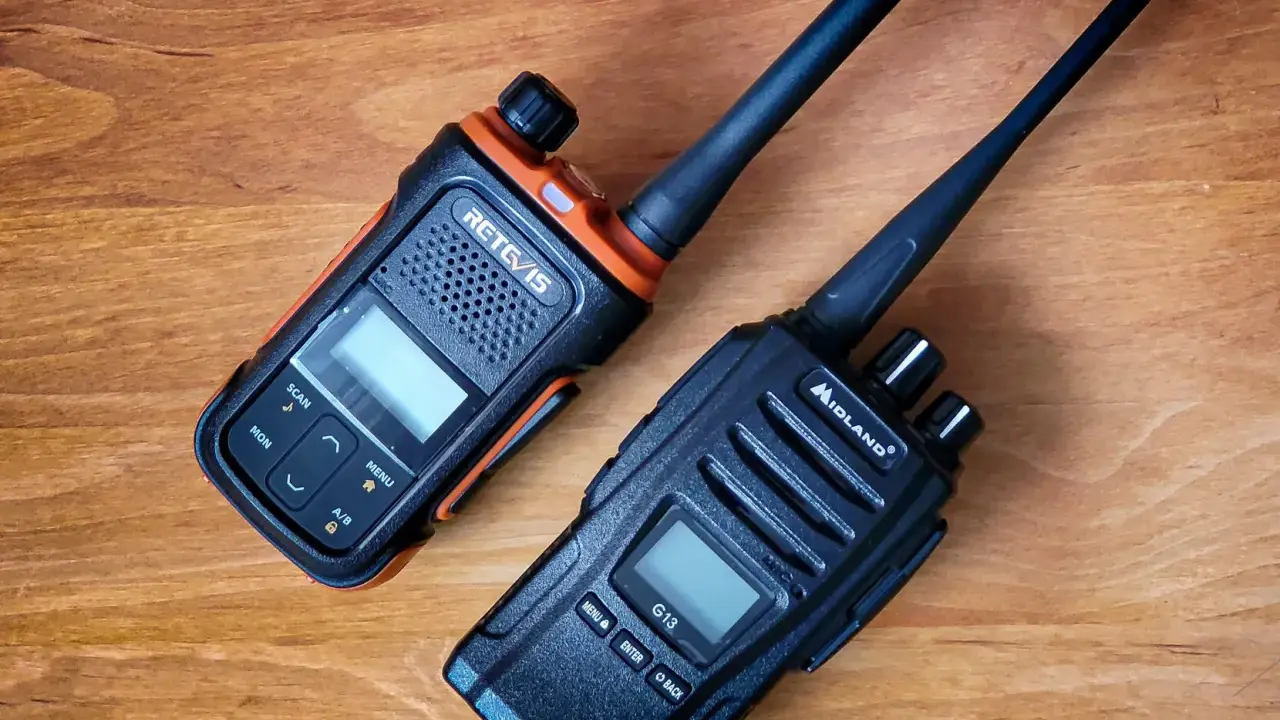 Dwa radiotelefony, jeden pomarańczowo-czarny RETCIS, drugi czarny Midland, leżą na drewnianym blacie.