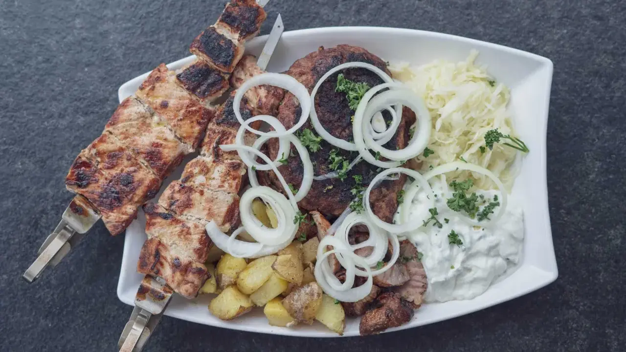 Ein Teller mit gegrilltem Fleisch, Kartoffeln und Krautsalat, garniert mit Zwiebelringen. Ein authentisches Souvlaki Rezept original.