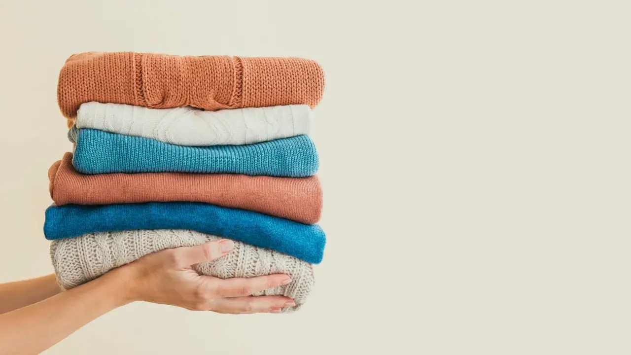 Hände halten einen Stapel bunter Pullover. Eine gute Idee für waschmittel ersatz, wenn man die Kleidung schonend behandeln möchte.