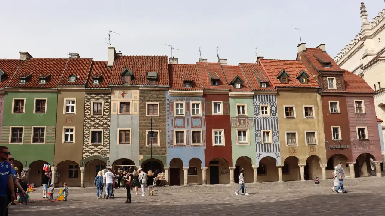 Kolorowe kamienice na Starym Rynku w Poznaniu, gdzie kwitnie rozrywka. Ludzie spacerują po bruku, podziwiając architekturę.