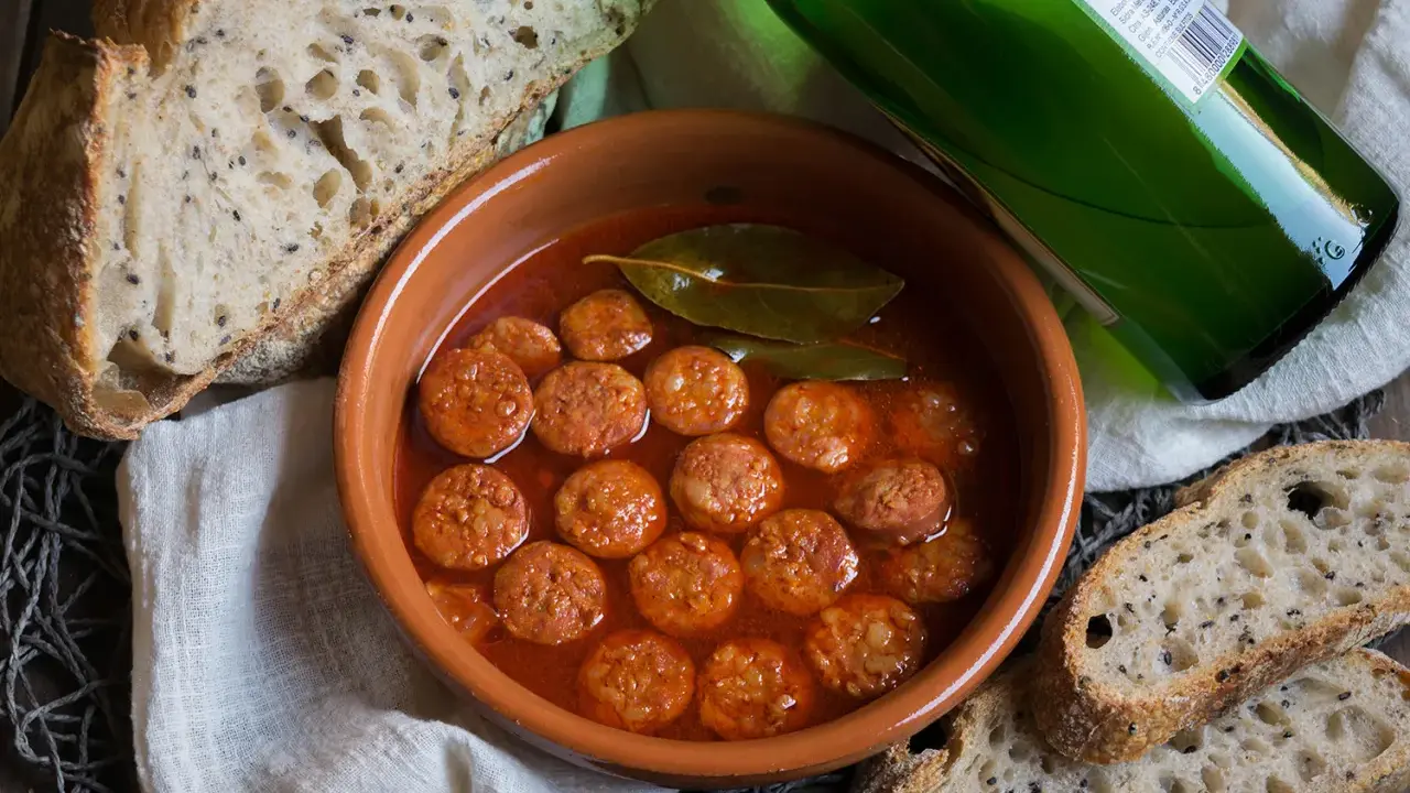 Chorizo a la sidra en cazuela de barro, acompañado de pan rústico y una botella de sidra verde.
