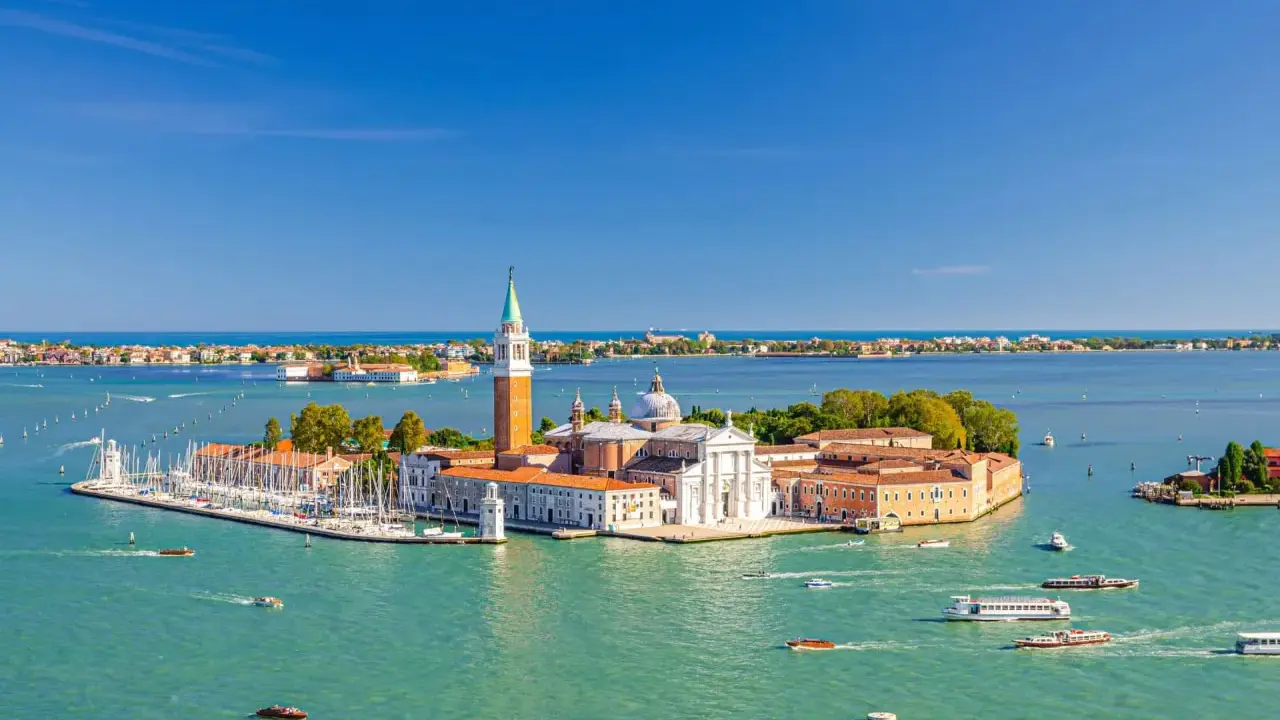 Vue aérienne de Venise, le campanile San Giorgio Maggiore se dresse fièrement sur son île, entouré d'eaux turquoise et de voiliers.