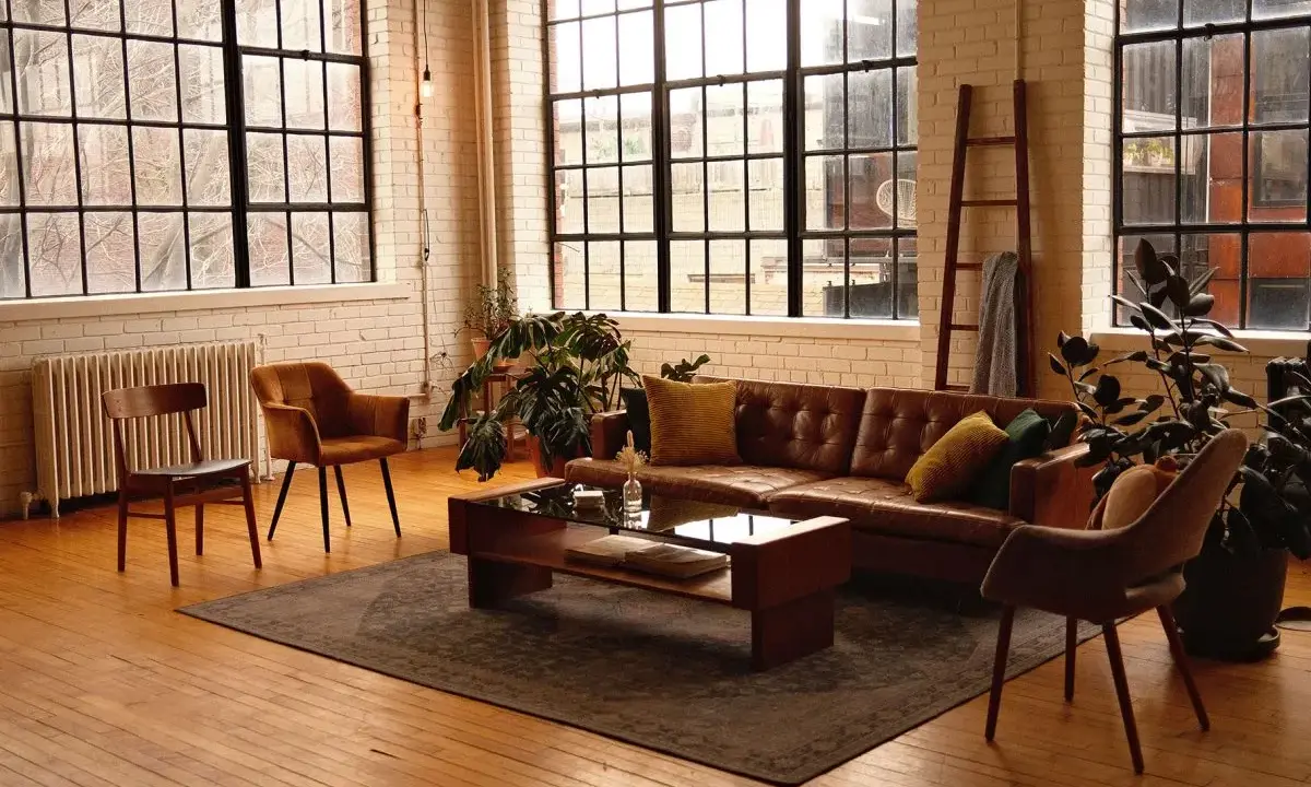 Przytulny salon w stylu loft aranżacje. Brązowa skórzana kanapa, drewniane meble i duże okna tworzą ciepłą atmosferę.