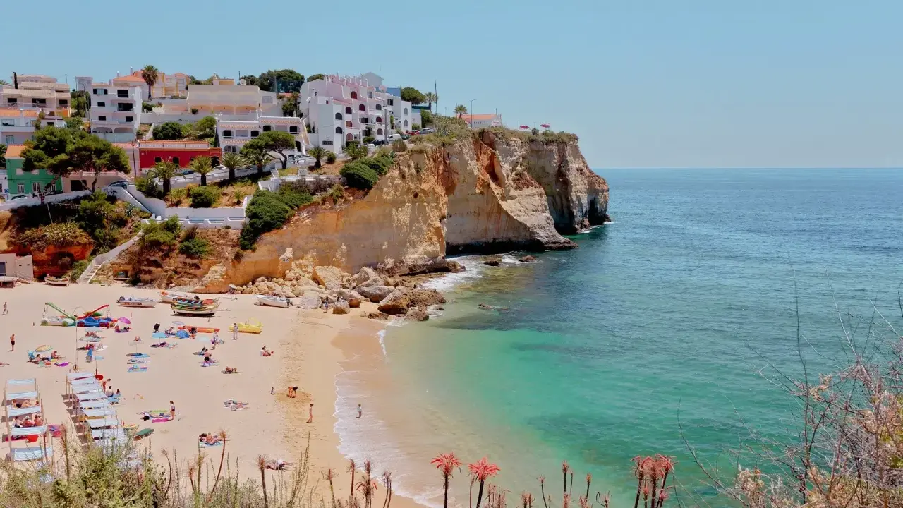 Sonnige Küste Portugals mit weißem Strand, türkisfarbenem Meer und Häusern auf den Klippen. Perfekt für eine Portugal Wetter Jahresübersicht.