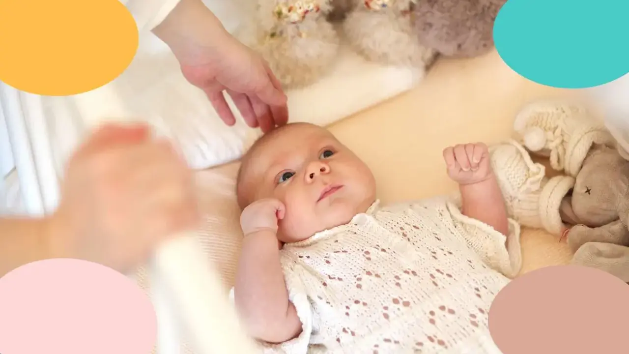 Un bebé despierto en su cuna, con una mano acariciándole la cabeza. Parece que mi bebe tarda mucho en dormirse.