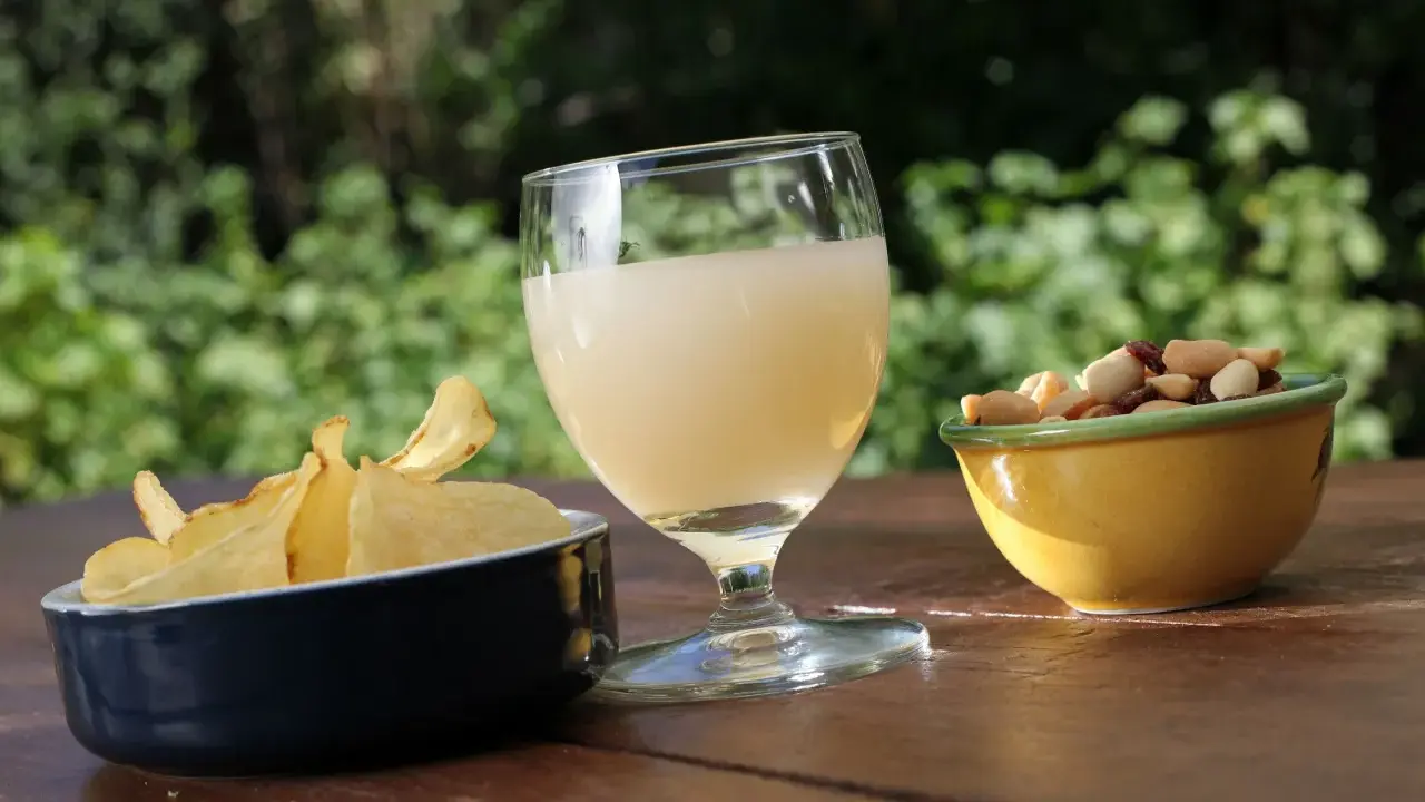 Verre de boisson claire, chips croustillantes et mélange de fruits secs, une spécialité PACA pour un apéritif ensoleillé.