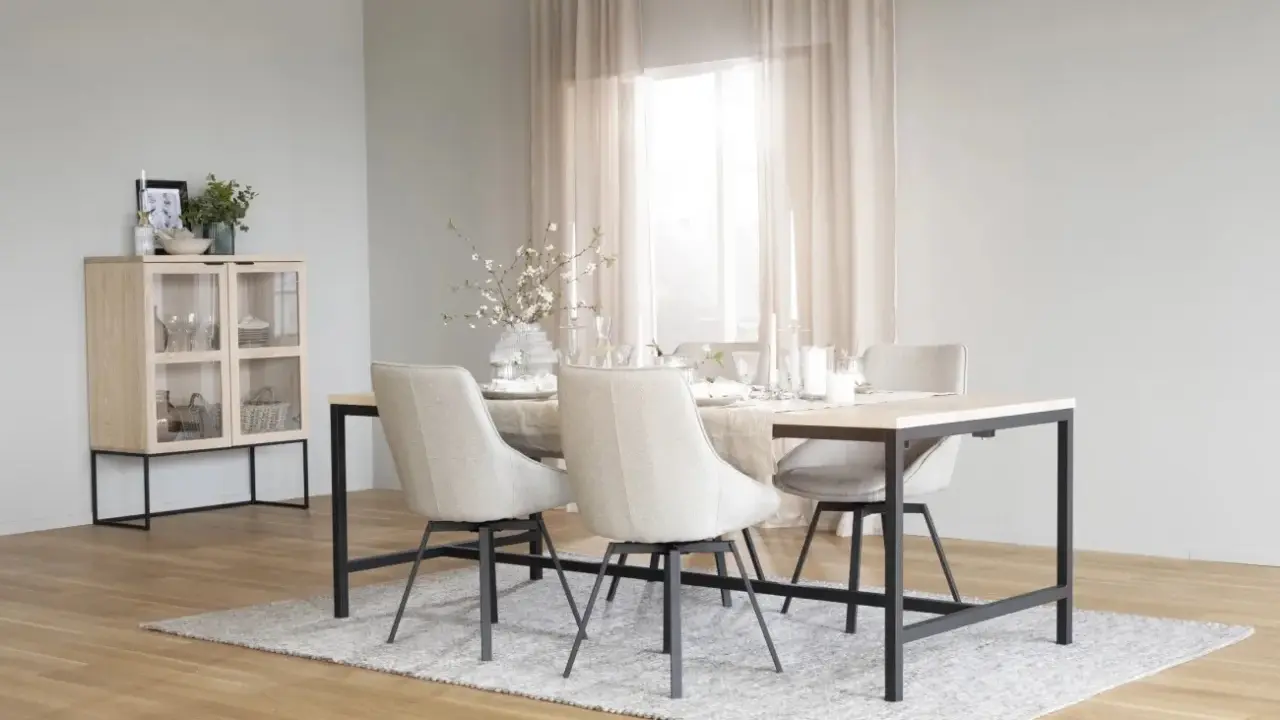 Ett ljust och luftigt rum med matbord och stolar i nordisk design. Ett vitrinskåp i trä och metall står till vänster.