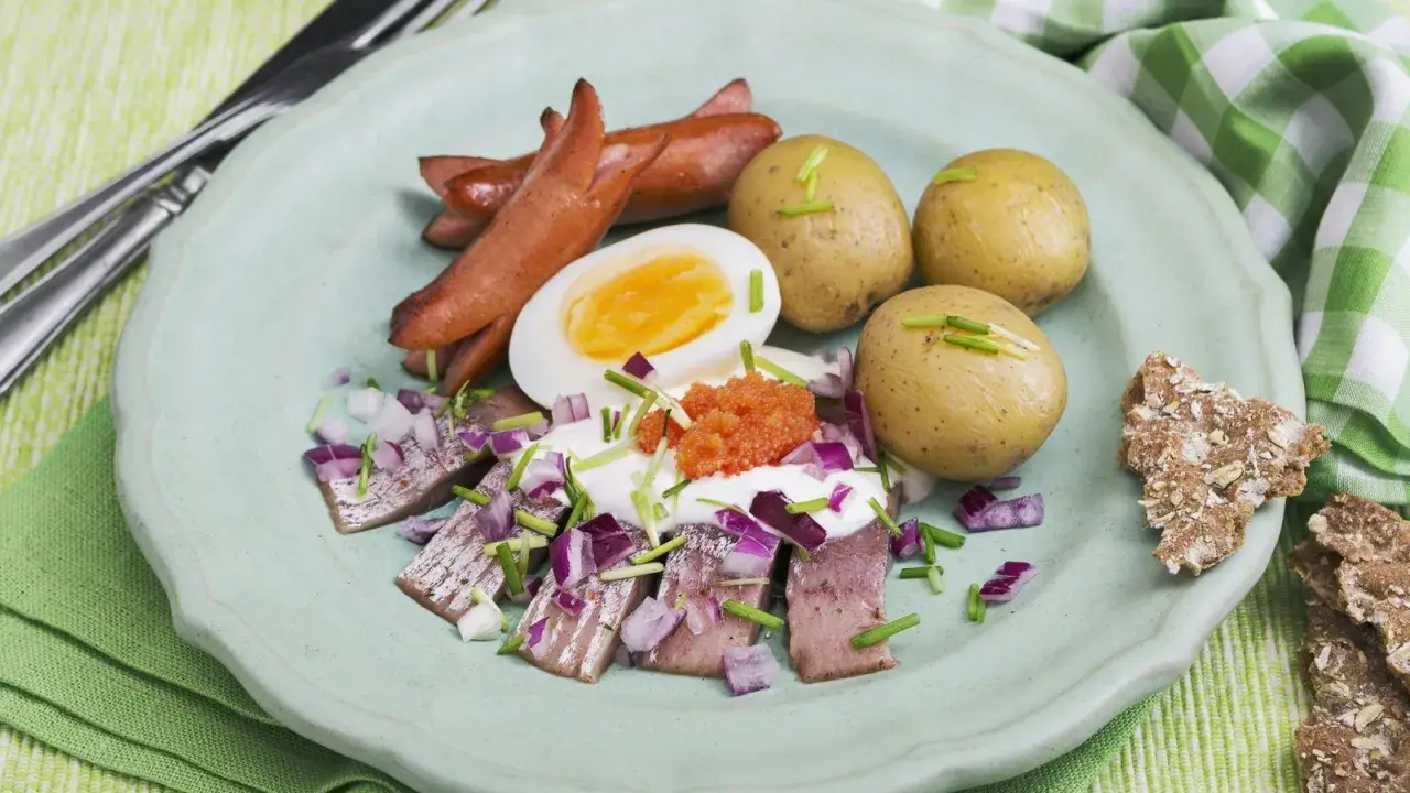 En tallrik med sill, ägg, prinskorv, potatis och rom. En härlig påskbord mat som ser utsökt ut.
