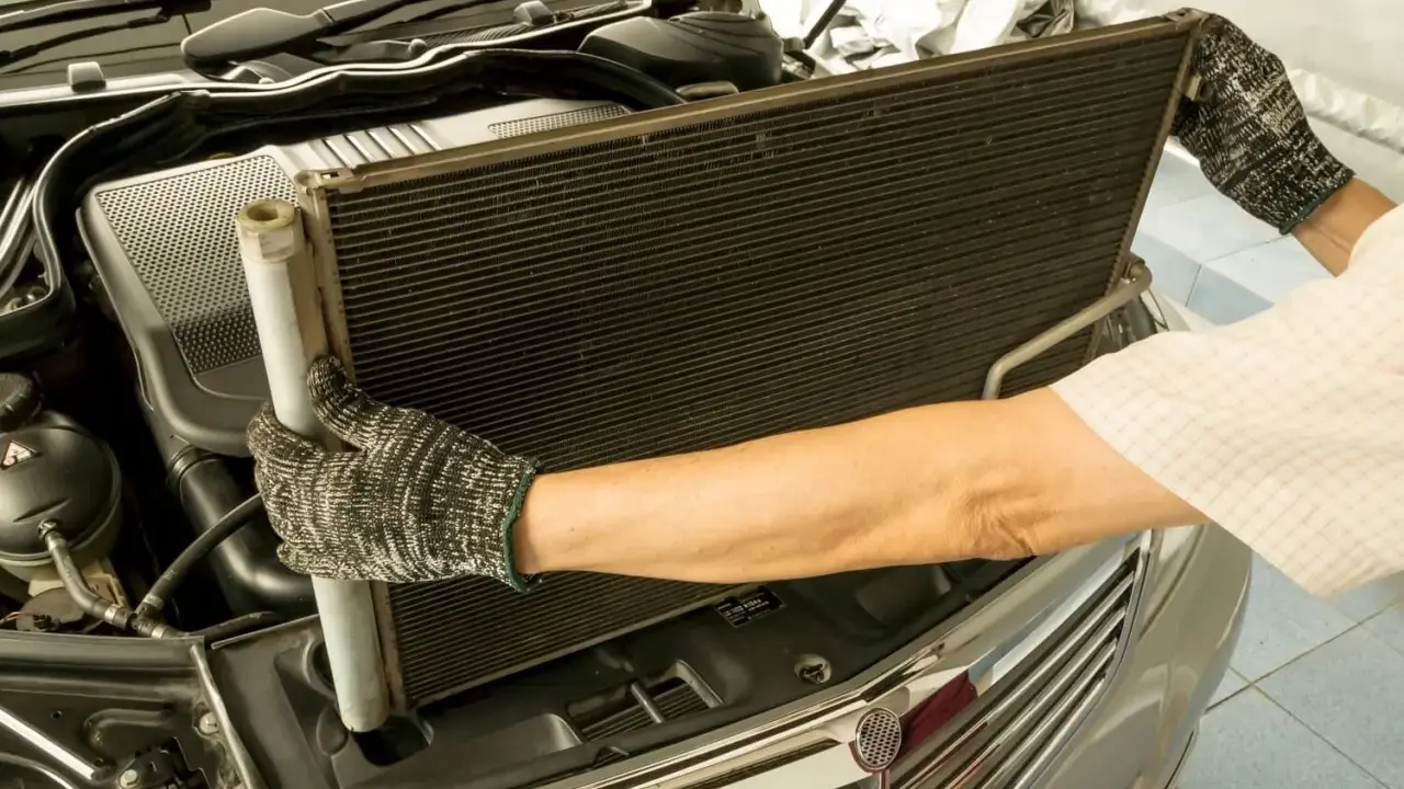 Mechanik w rękawicach wyjmuje skraplacz klimatyzacji z samochodu.