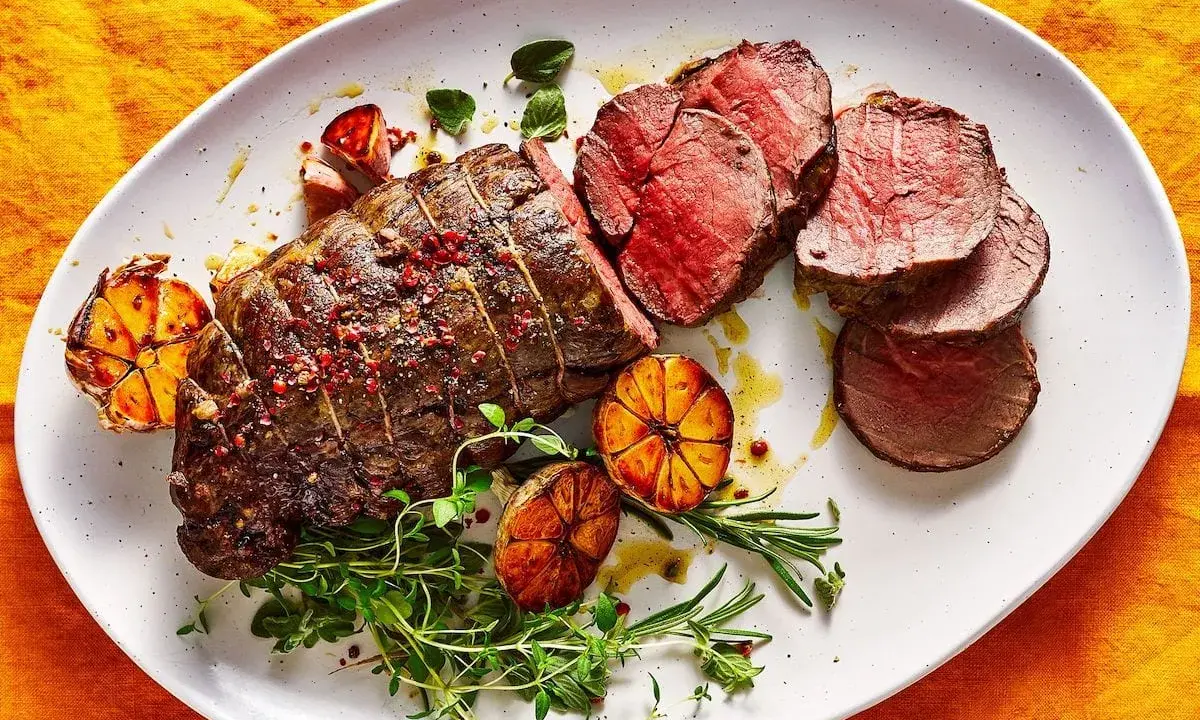 Roast beef al horno jugoso y tierno, servido con ajos asados y hierbas frescas.
