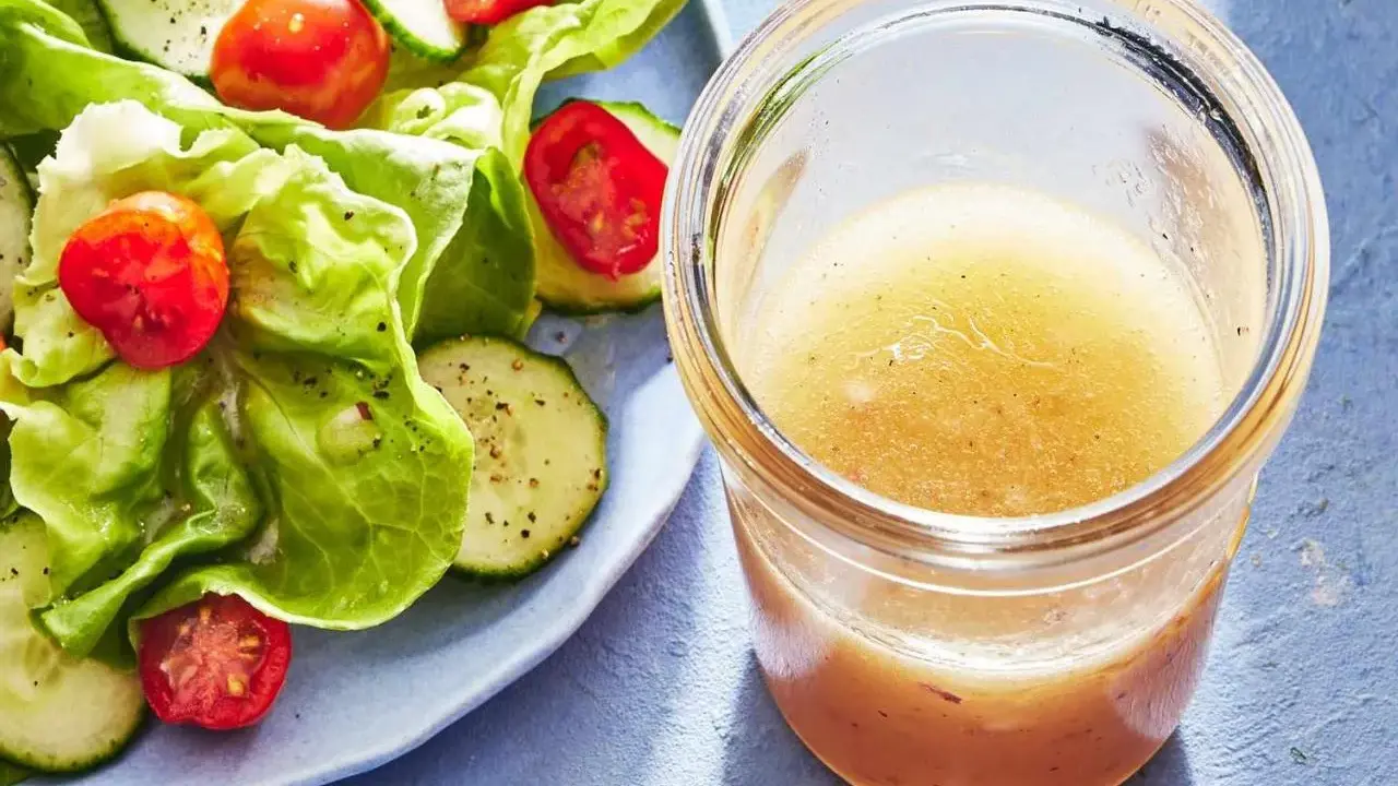 En burk med hemlagad salladsdressing bredvid en fräsch sallad med gurka och tomater. Ett perfekt salladsdressing recept för en lätt lunch.