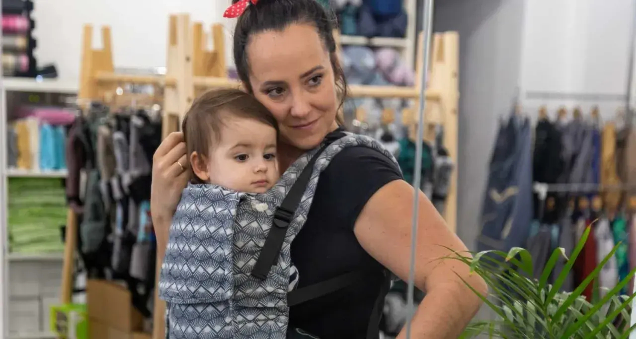 Mama wybiera jakie nosidełko dla 5 miesięcznego niemowlaka. Dziecko w nosidle z wzorem.