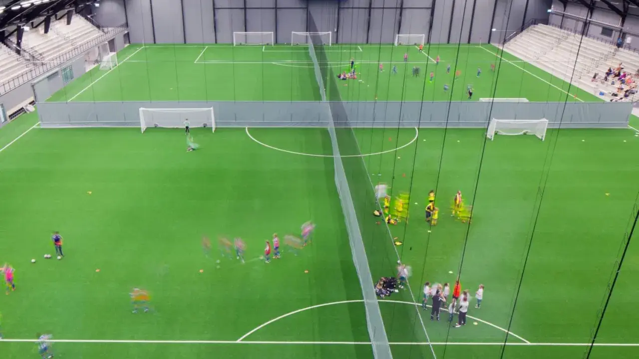 Barn tränar fotboll på en grön konstgräsplan i Prioritet Serneke Arena. Publik sitter på läktaren.
