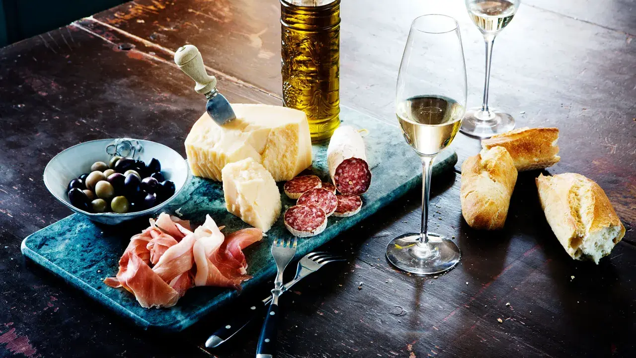 En härlig italiensk buffé med ost, salami, prosciutto, oliver, bröd och ett glas vitt vin, kanske en riesling druva.