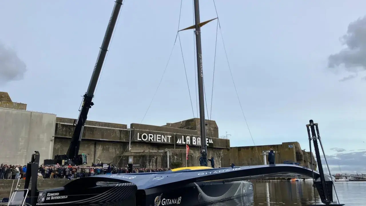 Le trimaran Gitana 18, prêt pour l'aventure, est soulevé par une grue à Lorient. Une foule nombreuse est rassemblée pour admirer ce géant des mers.