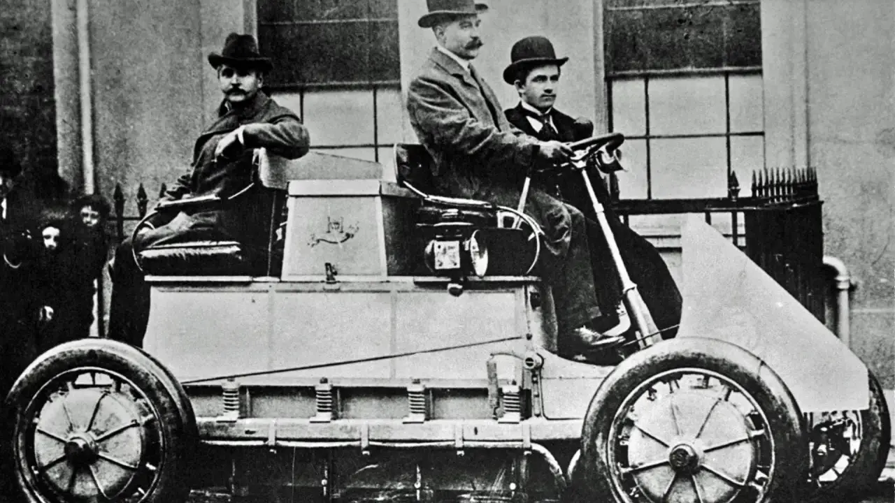 Hombres con sombreros posan en el primer coche eléctrico de la historia, un vehículo pionero de finales del siglo XIX.