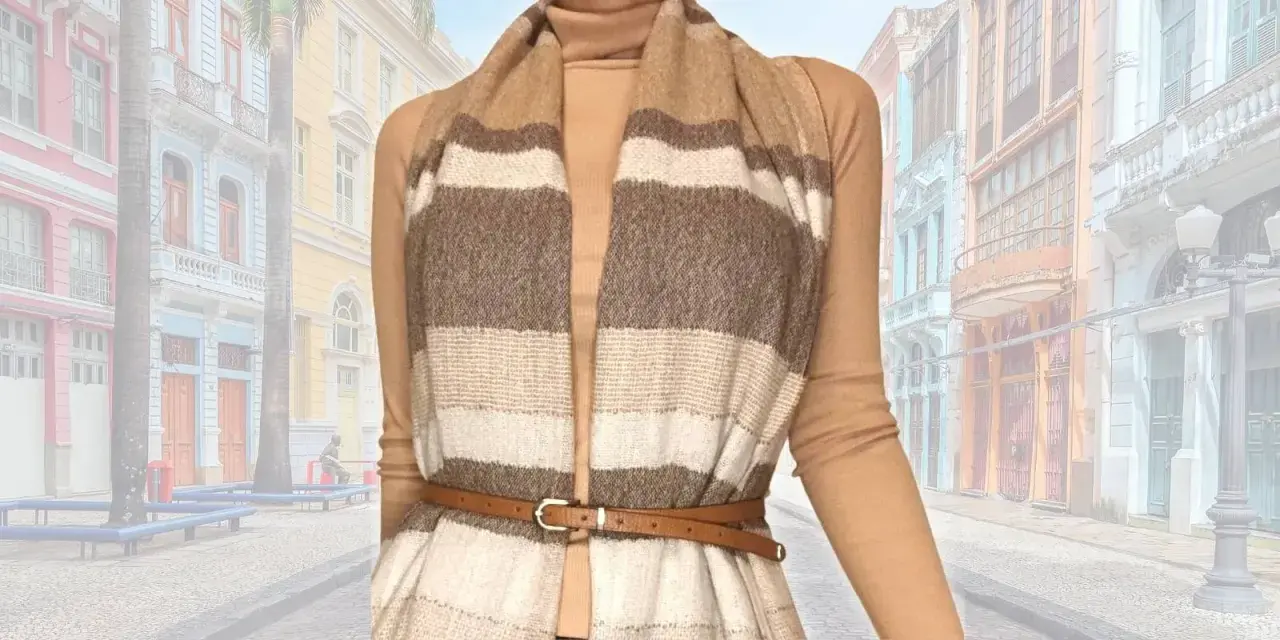 Modello che mostra come indossare una sciarpa grande a righe, abbinata a un dolcevita e una cintura sottile, con uno sfondo di edifici colorati.