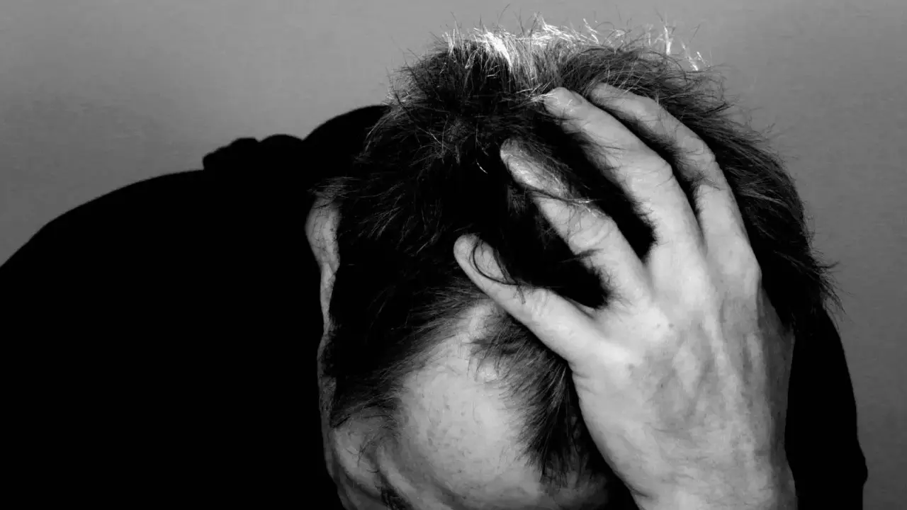 Uomo con mano tra i capelli, ombra scura sul volto. Potrebbe rappresentare il peso di una diagnosi di linfoma cutaneo.
