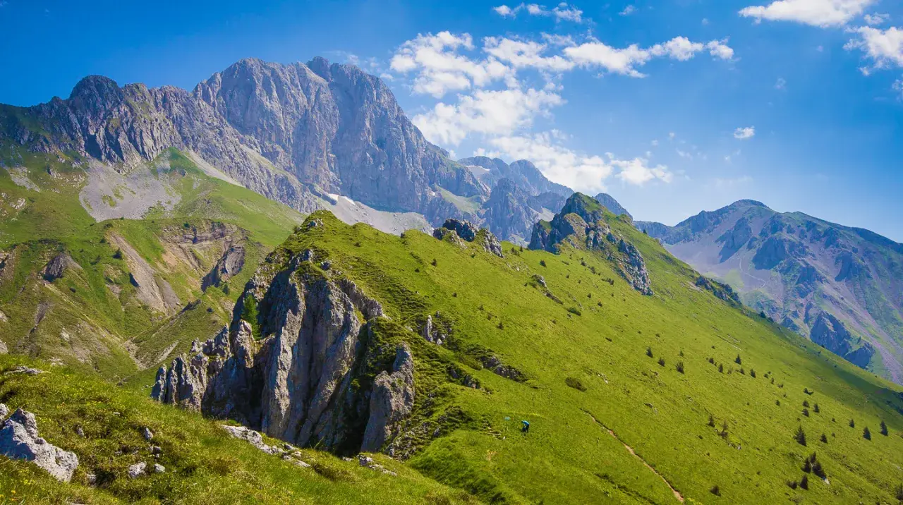 Prati verdi e sentieri invitano a **passeggiate facili** in Val Seriana, con maestose cime sullo sfondo sotto un cielo azzurro.