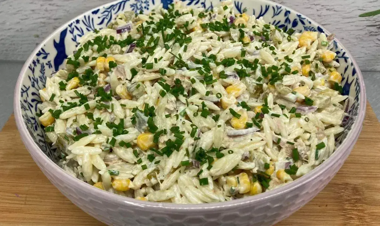 Pyszna sałatka z tuńczykiem, makaronem orzo, kukurydzą i szczypiorkiem, podana w ozdobnej misce.