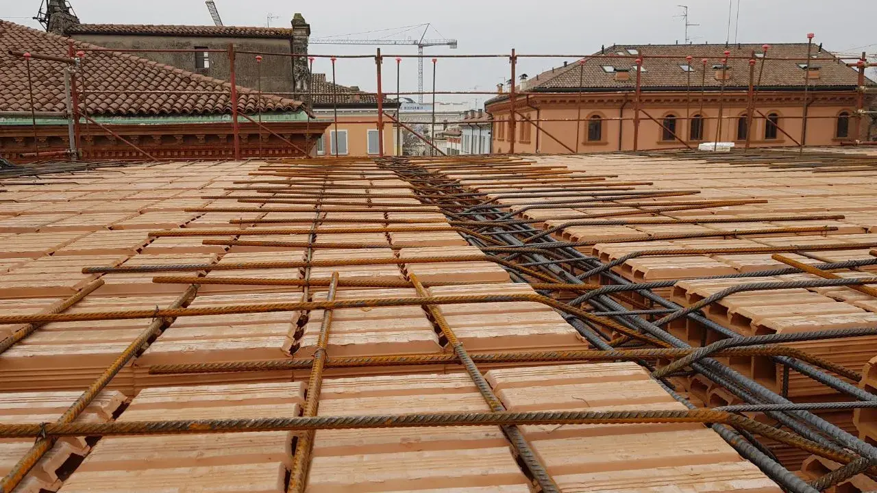 Posa di armature su tavelloni in laterizio, con sullo sfondo facciate in pietra e mattoni di edifici storici.