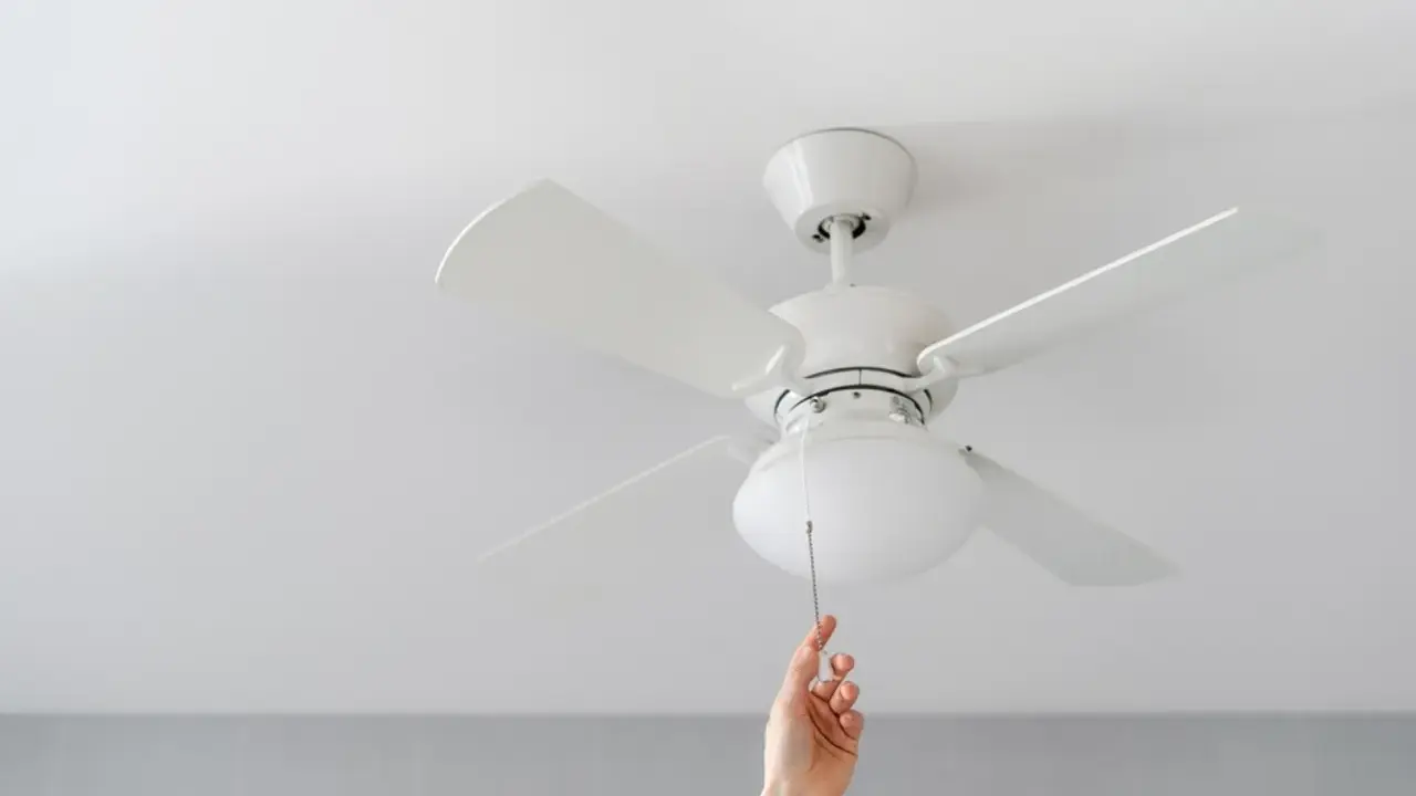 Mano tira de la cadena de un ventilador de techo pladur blanco, iluminando la habitación.
