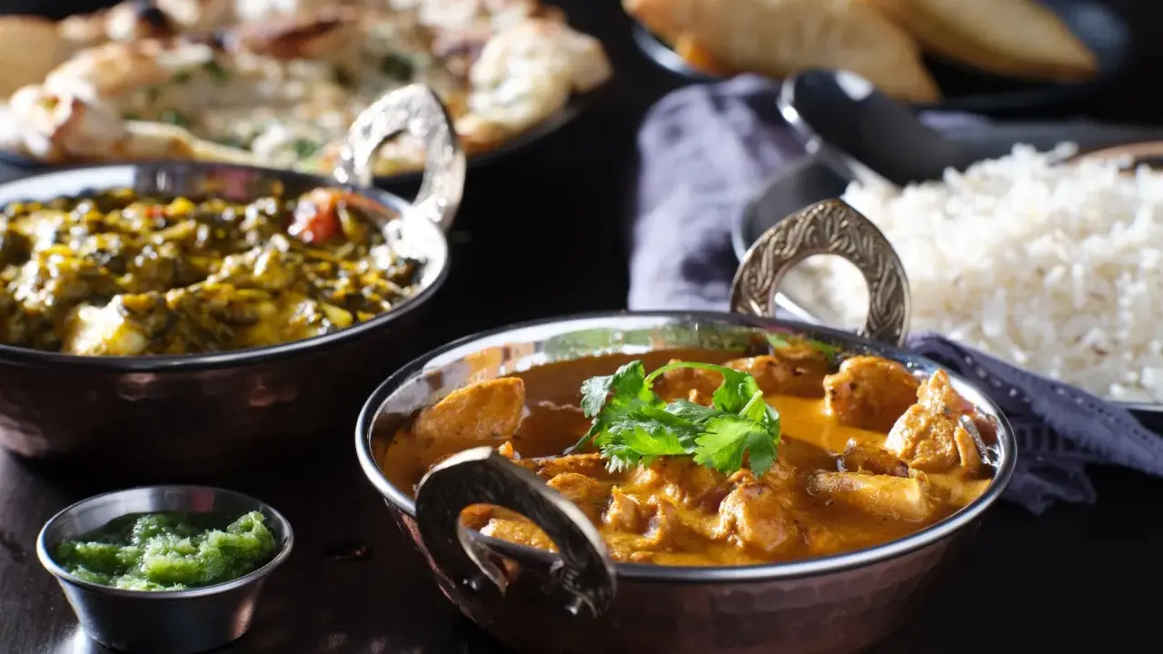 Delicioso pollo tikka masala cremoso, acompañado de arroz basmati, pan naan y una guarnición verde.