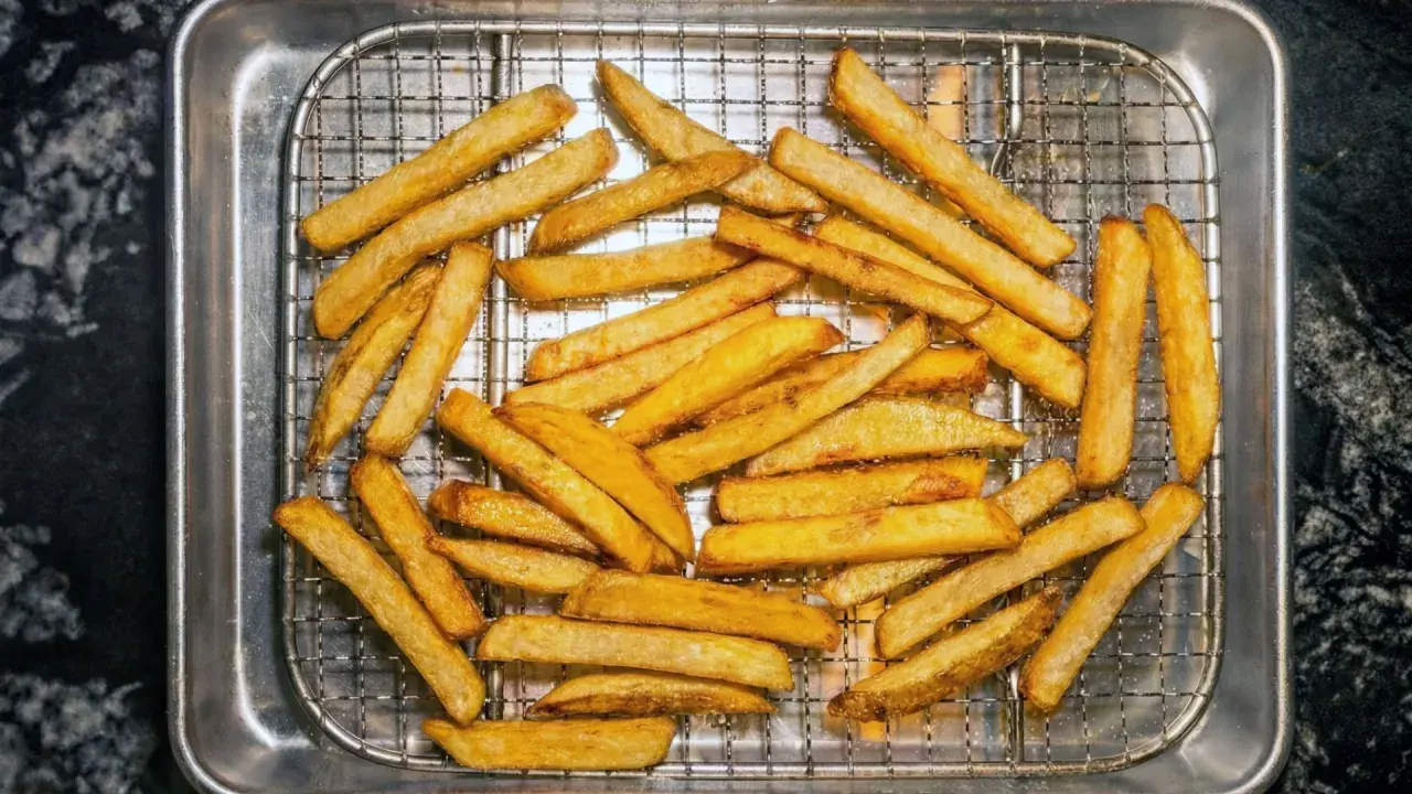 En hög med gyllene, krispiga pommes frites ligger på ett galler i en plåt. Perfekt för en snabb fika!