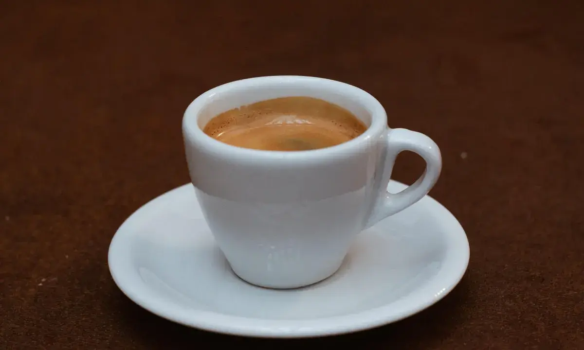 Ein kleiner weißer Becher mit cremigem, doppeltem Espresso, italienisch zubereitet, steht auf einer Untertasse.