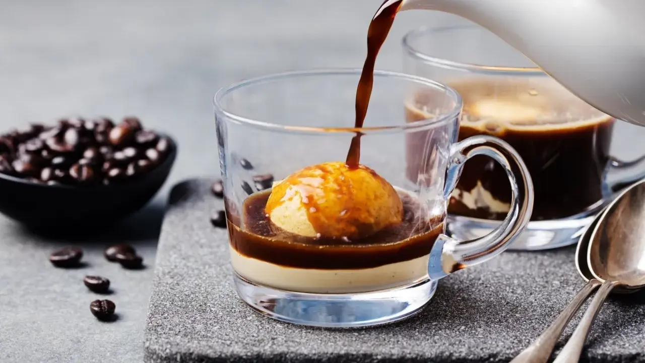 Heißer Espresso fließt über eine Kugel Vanilleeis in einem Glas. Ein köstlicher Affogato al caffè, bereit zum Genießen.