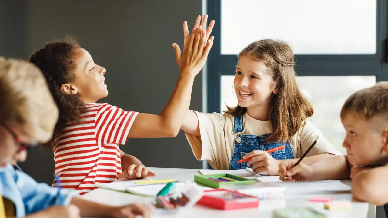 Kinder geben sich High-Five bei einer Gruppenarbeit. Sie lernen und arbeiten zusammen, was tolle Gruppenarbeit Methoden zeigt.